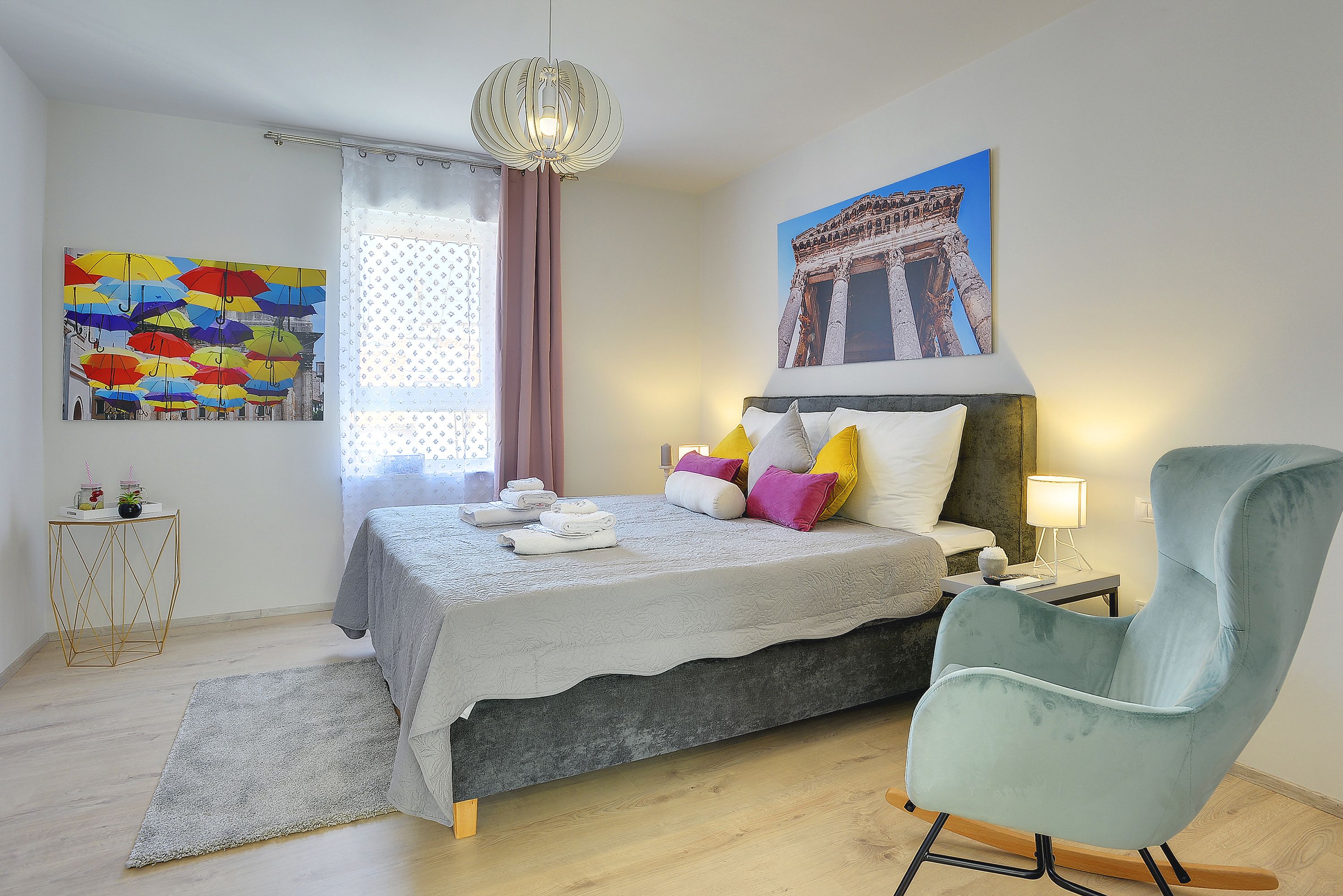 A bedroom with a bed, a chair, a lamp, and artwork on the walls.