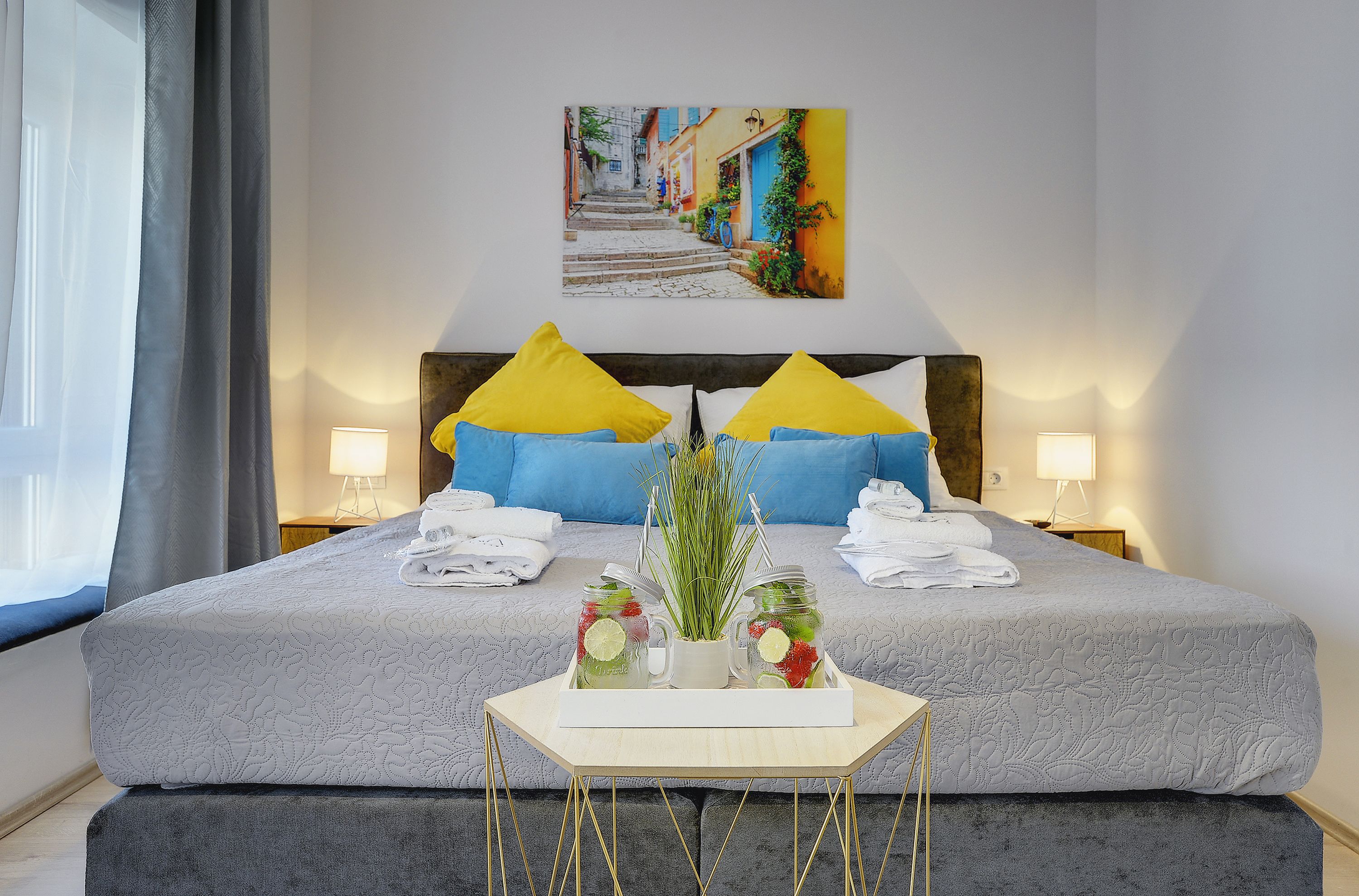 Habitación de hotel con una cama grande, dos almohadas, una mesita de noche con un florero y un cuadro en la pared.