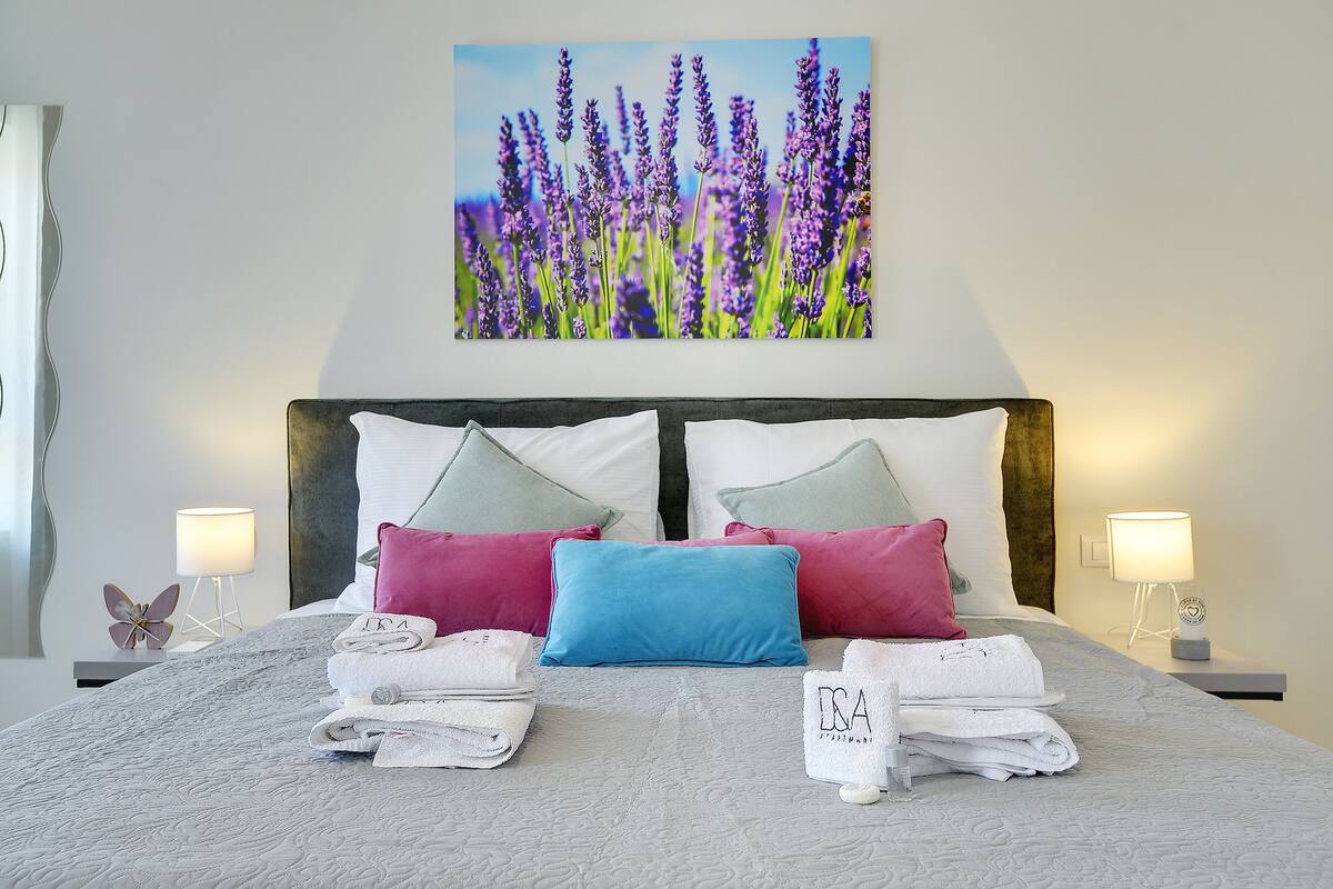 A neatly made bed with a floral artwork above it, two bedside lamps, and a decorative butterfly on the nightstand.