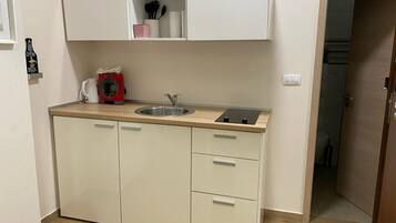 Una kitchenette compacta con un lavabo, una tetera roja y un mueble pequeño.