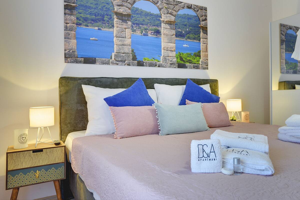 A neatly made bed with a headboard, pillows, and a nightstand with a lamp.