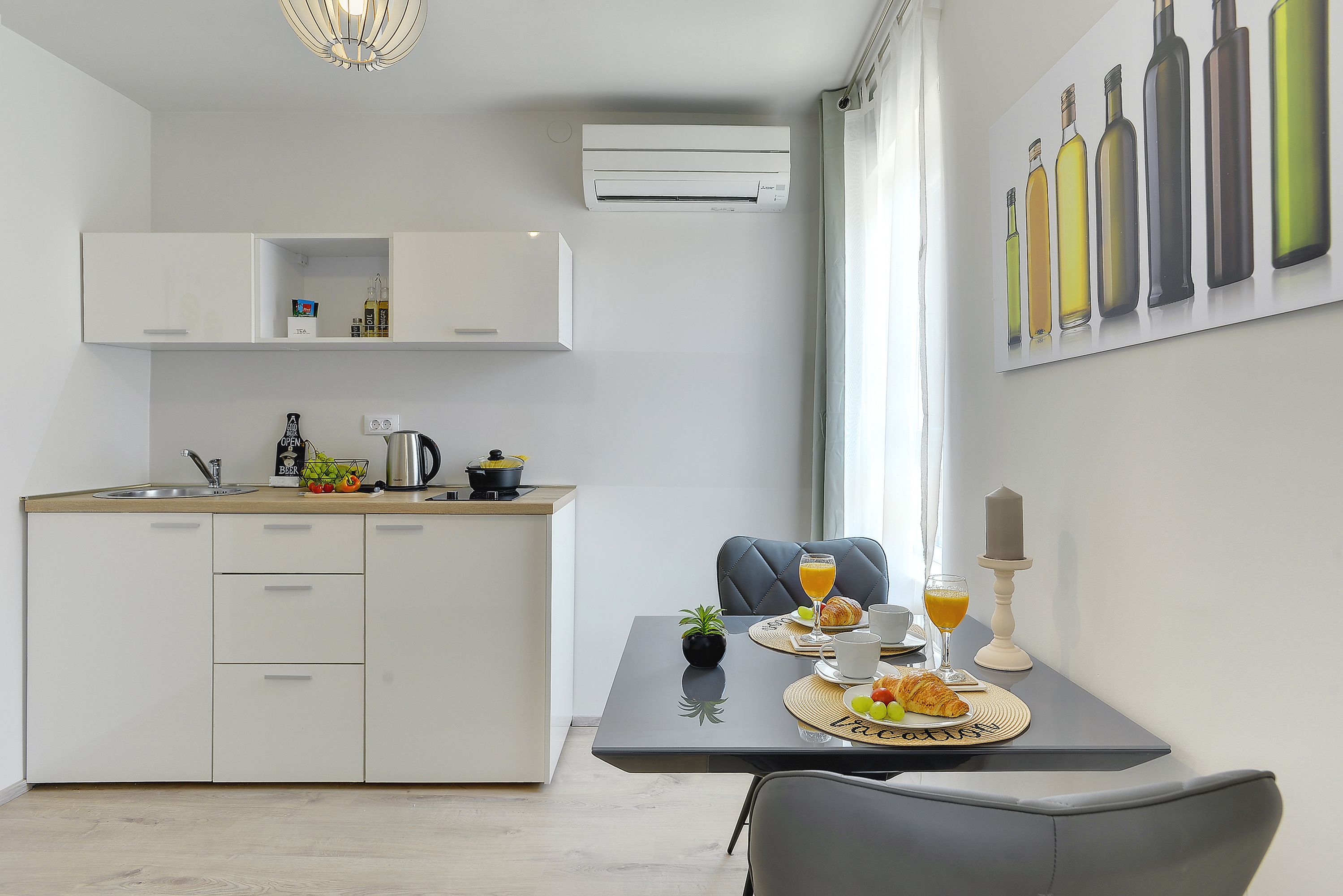 A modern kitchen with white cabinets, a dining table with breakfast items, and a large window with curtains.