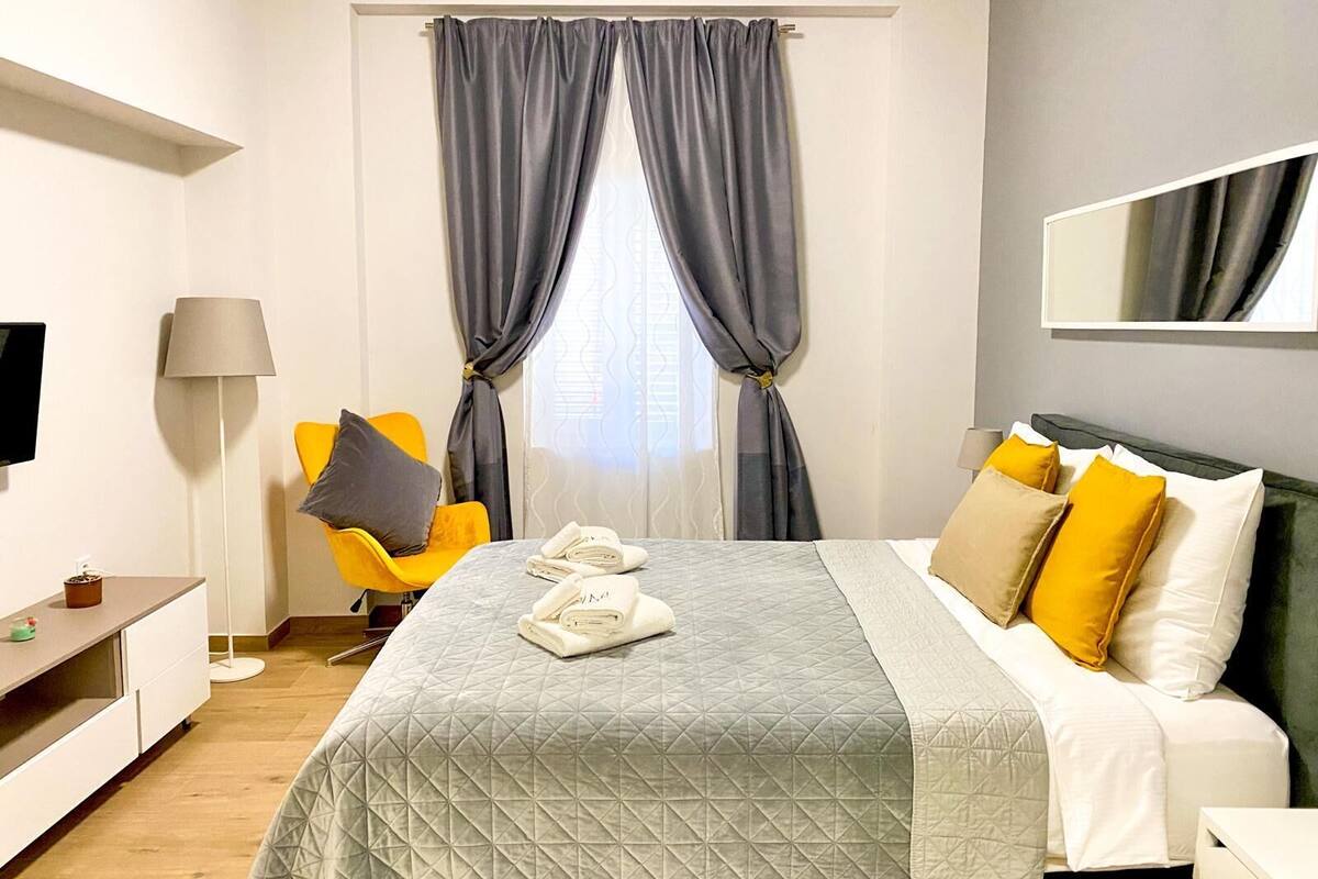 A hotel room with a bed, a desk, a chair, a lamp, and a window with curtains.