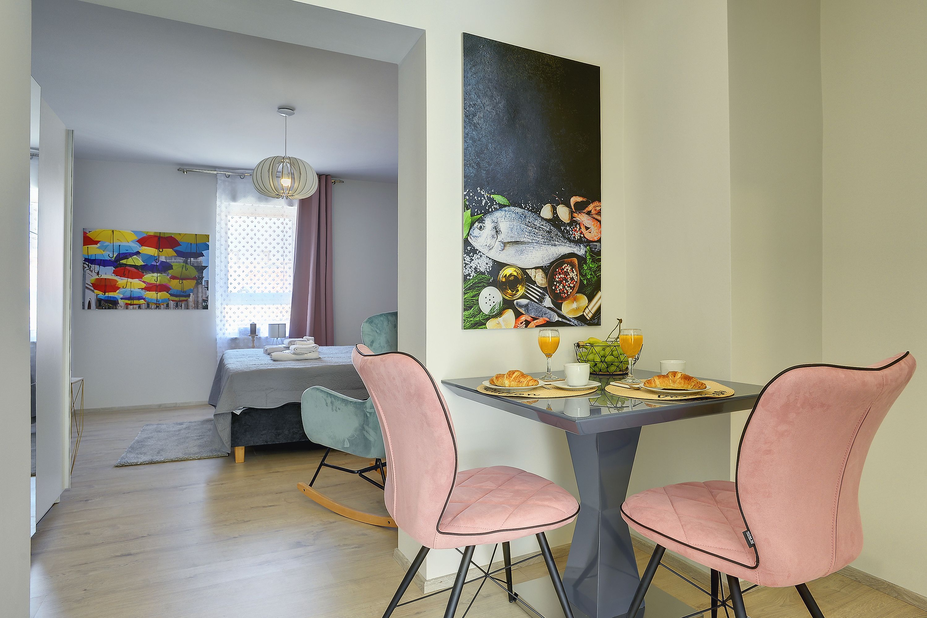 Un comedor con una mesa dispuesta para dos personas, una cama al fondo y una obra de arte colorida en la pared.