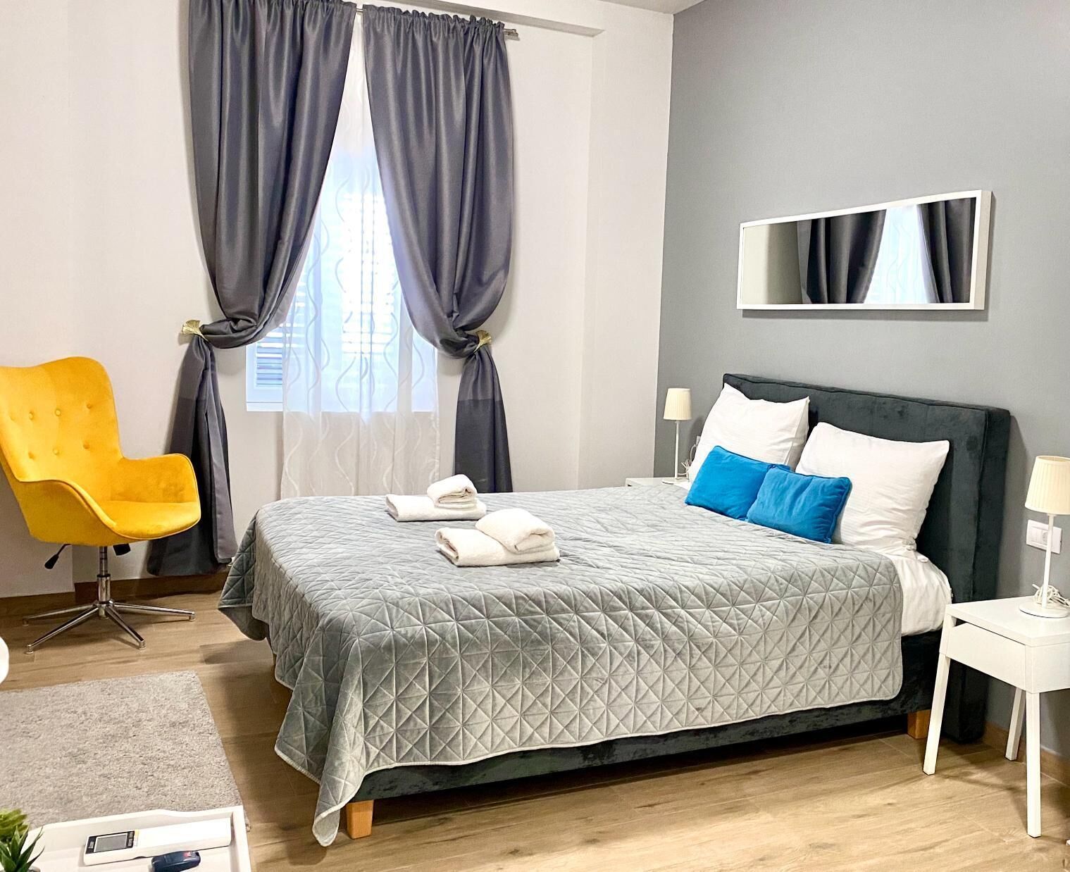 A hotel room with a bed, a chair, a bedside table, and a mirror.