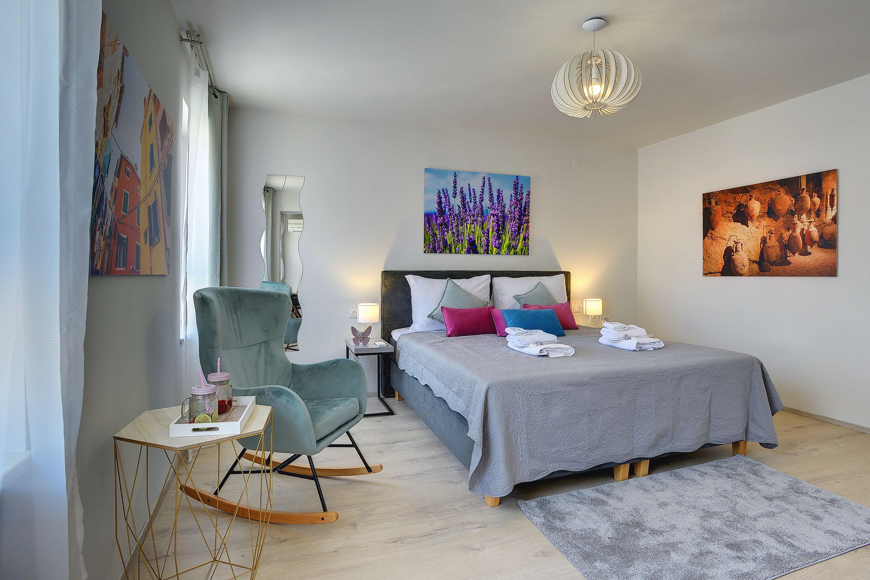A bedroom with a bed, a chair, a small table with a tray, and two wall-mounted lamps.