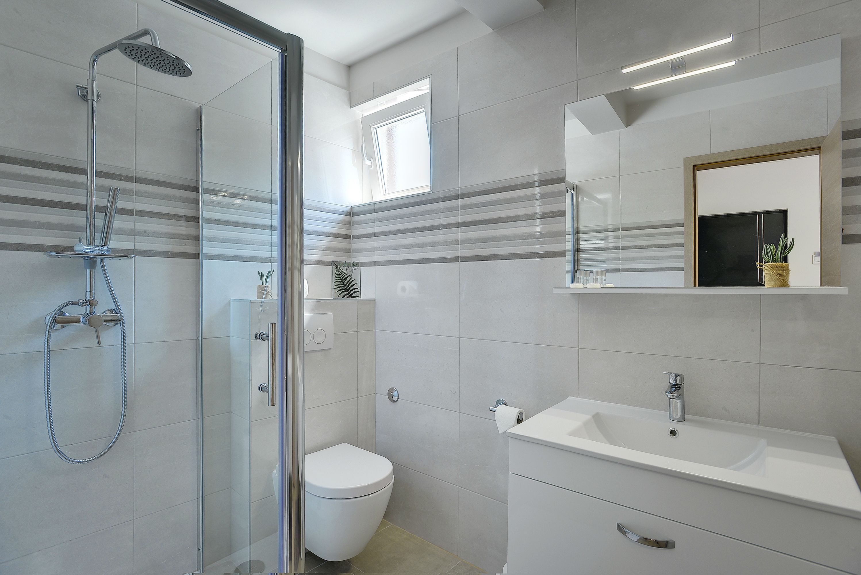 A modern bathroom with a glass-enclosed shower, a toilet, and a sink with a mirror above.
