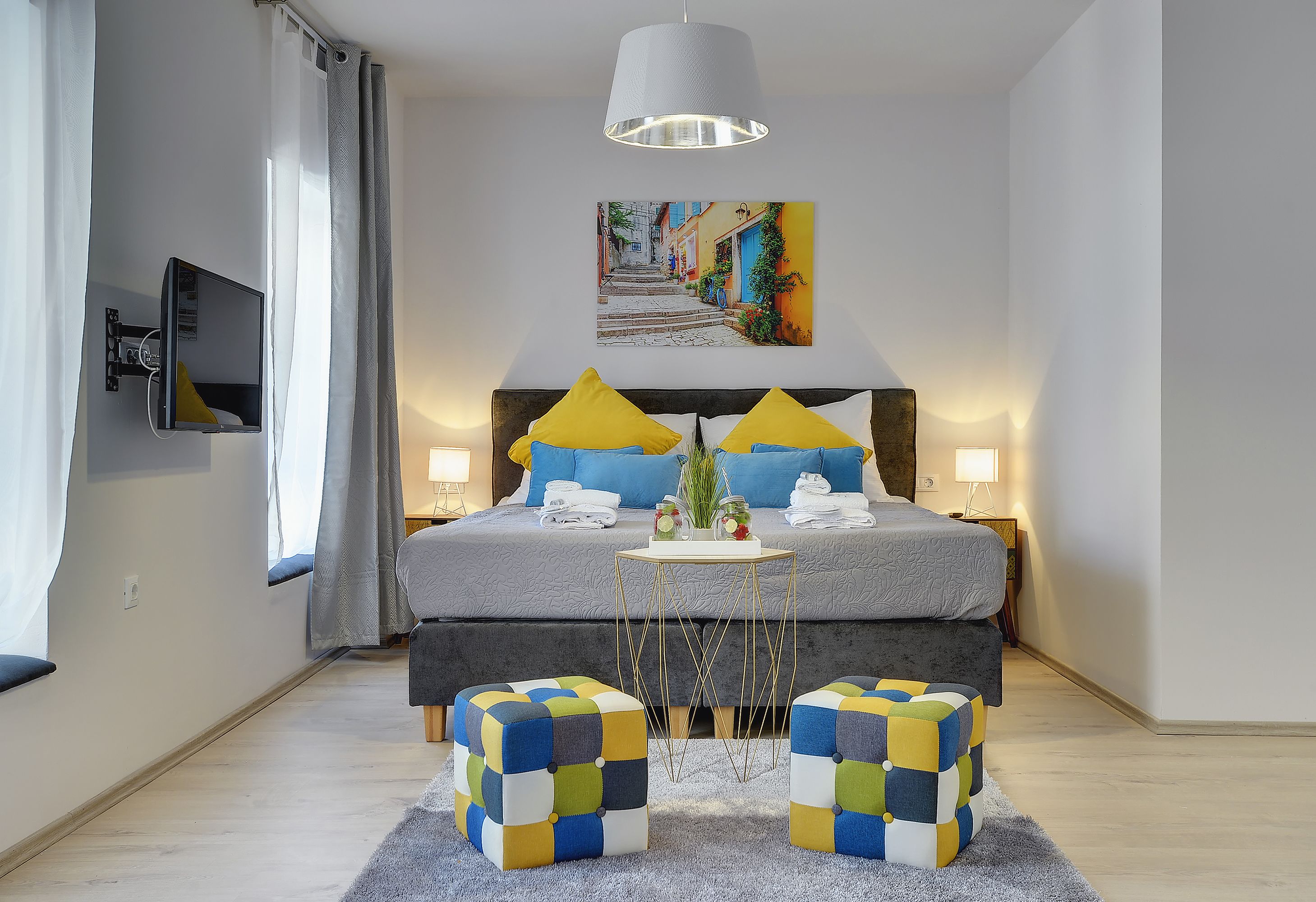A modern bedroom with a bed, bedside lamps, a mounted TV, and a painting on the wall.