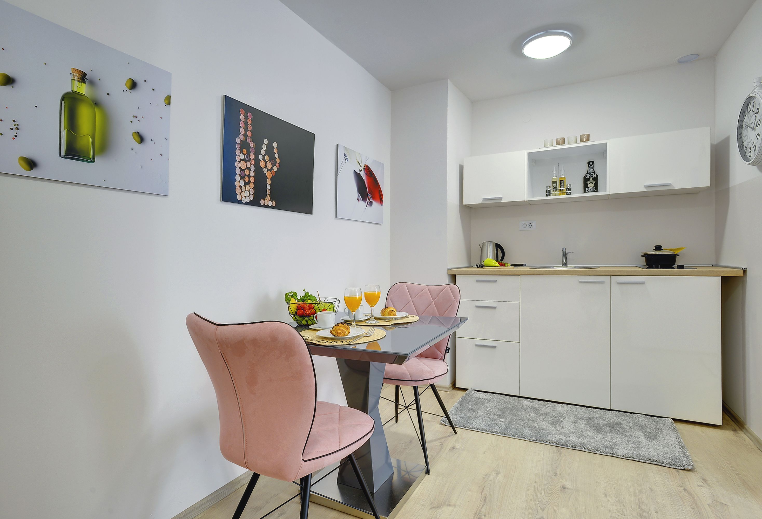 Una cocina moderna con armarios blancos, una mesa de comedor con sillas rosadas y obras de arte en las paredes.