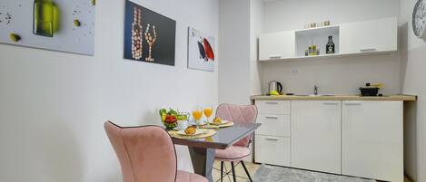 Una cocina moderna con armarios blancos, una mesa de comedor con sillas rosadas y obras de arte en las paredes.