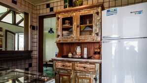 A kitchen with a white refrigerator, wooden cabinets, and a tiled backsplash. - Casa Cantinho em Ilhabela (Ilhabela)