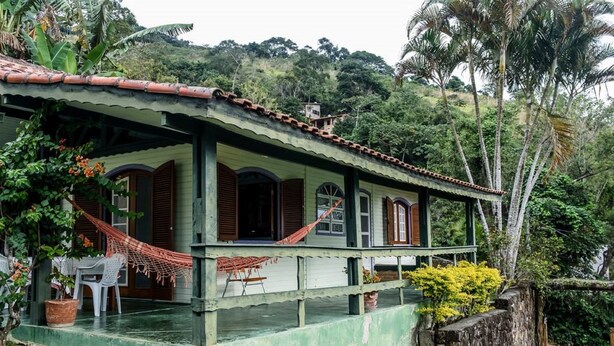 A house with a porch, a hammock, and a small table with chairs. - Casa Cantinho em Ilhabela (Ilhabela)