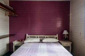 A bedroom with a bed, two nightstands, a lamp, and a shelf with colorful hangers. - Casa Cantinho em Ilhabela (Ilhabela)