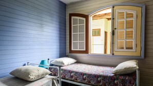A small room with two single beds, a blue wall, and a window with shutters. - Casa Cantinho em Ilhabela (Ilhabela)