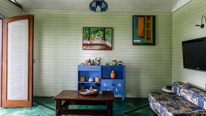 A room with a wooden table, a blue cabinet with decorative items, a sofa with patterned cushions, and a painting on the wall. - Casa Cantinho em Ilhabela (Ilhabela)