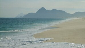 Una playa con arena dorada y un mar tranquilo, con montañas al fondo.