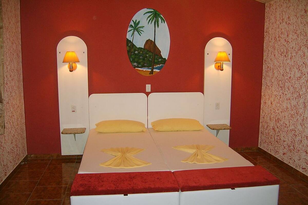 Una cama doble con dos almohadas, una pared de acento roja y dos lámparas de pared.