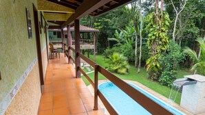 Un espacio al aire libre techado con piscina, rodeado de exuberante vegetación y una terraza de madera.