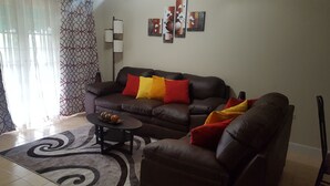 Un salon avec un canapé en cuir marron, un fauteuil assorti et une table basse. Il y a trois coussins sur le canapé et un sur le fauteuil. Un vase décoratif est posé sur la table basse.