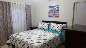 Une chambre à coucher comprenant un lit, une table de chevet, un téléviseur fixé au mur et une fenêtre avec des rideaux.