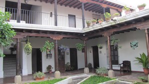 A courtyard with a wooden balcony, potted plants, and a stone fountain. - Suite El Nido (Antigua Guatemala)