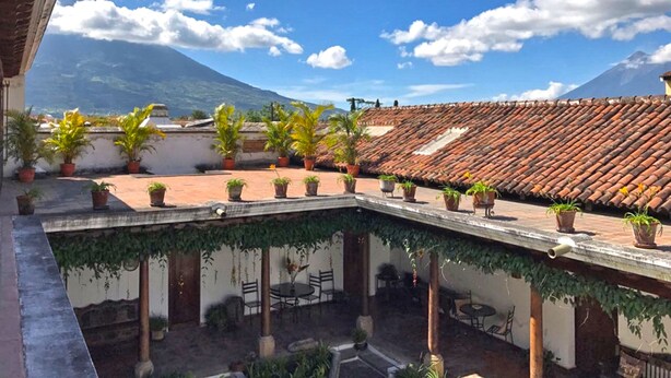 A courtyard with terracotta roof tiles, potted plants, and a view of a mountain. - Suite El Nido (Antigua Guatemala)