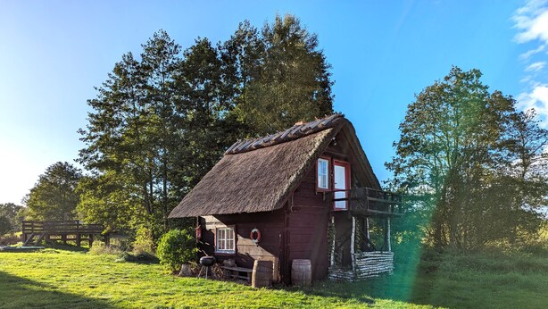 A rustic wooden house with a thatched roof, a wooden porch, and a small window.