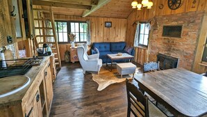 Interior rústico de una cabaña con paredes de madera, un sofá azul, una mesa de comedor y una chimenea.