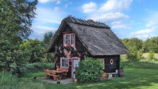 Una casa de madera rústica con techo de paja, un banco de madera y una pequeña mesa.