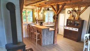 Una cocina rústica con una isla central, taburetes de madera, estufa a leña y refrigerador de estilo campestre.