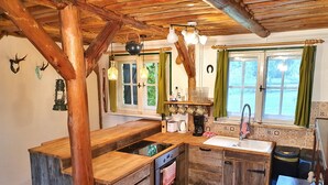 Una cocina rústica con armarios de madera, estufa empotrada, un lavamanos y una ventana con cortinas.