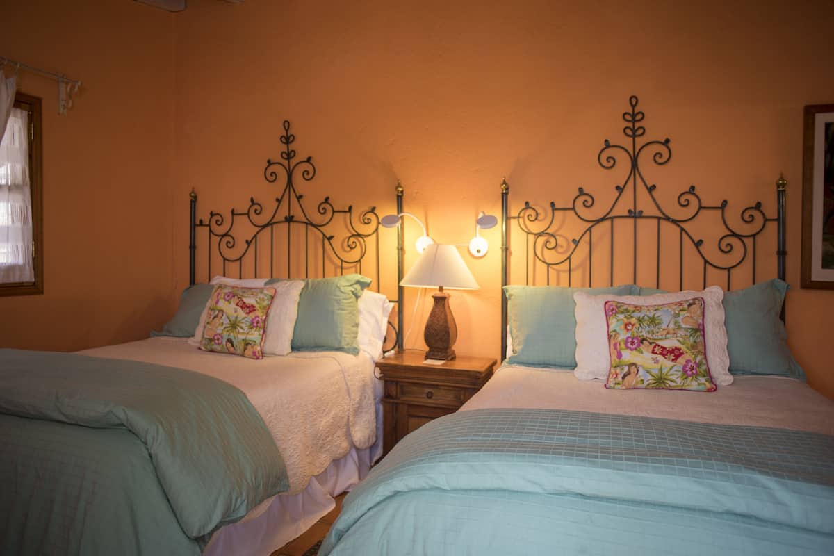 Une chambre à coucher avec deux lits, chacun doté d’une tête de lit au design distinct, une table de chevet avec une lampe et une fenêtre avec des rideaux.