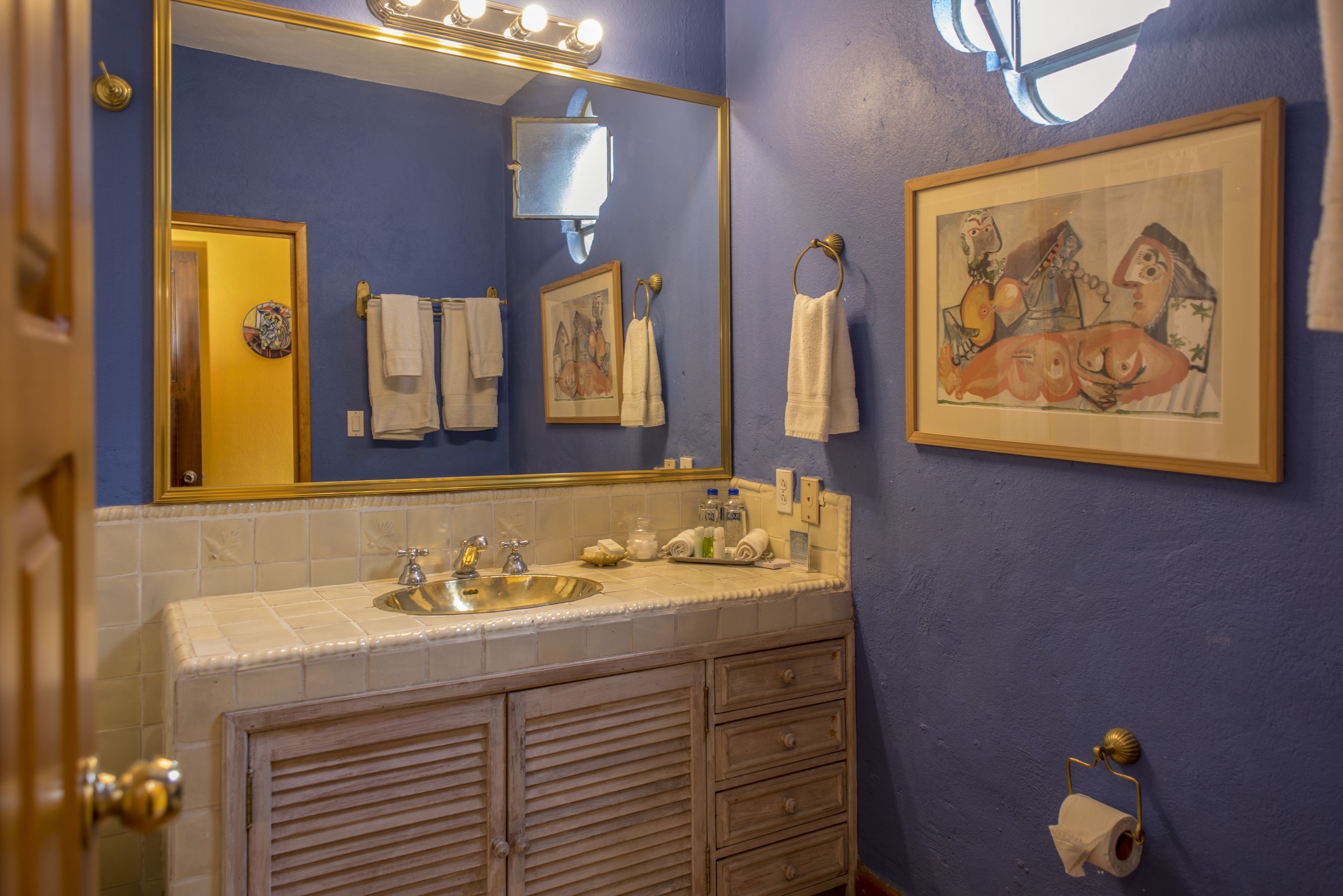 A bathroom with a sink, mirror, towels, and a painting on the wall.