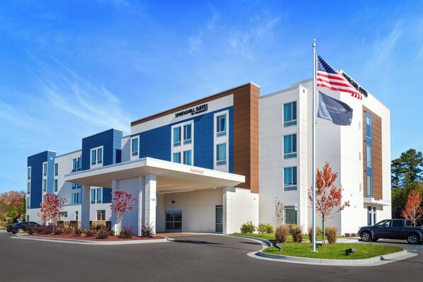 Un hotel moderno con fachada azul y blanca, un acceso cubierto y un asta con la bandera estadounidense.