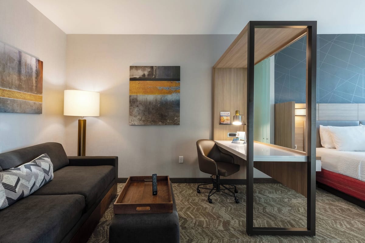 Een hotelkamer met een bank, bureau en bed. Op de muur hangt een schilderij, er staat een lamp en een dienblad met een afstandsbediening.