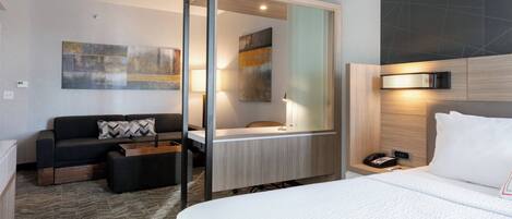 A modern hotel room with a large bed, a sofa, a desk, and a bathroom.