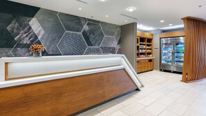 Uma área de recepção moderna com um balcão de madeira, parede com padrão hexagonal e um refrigerador cheio de bebidas.
