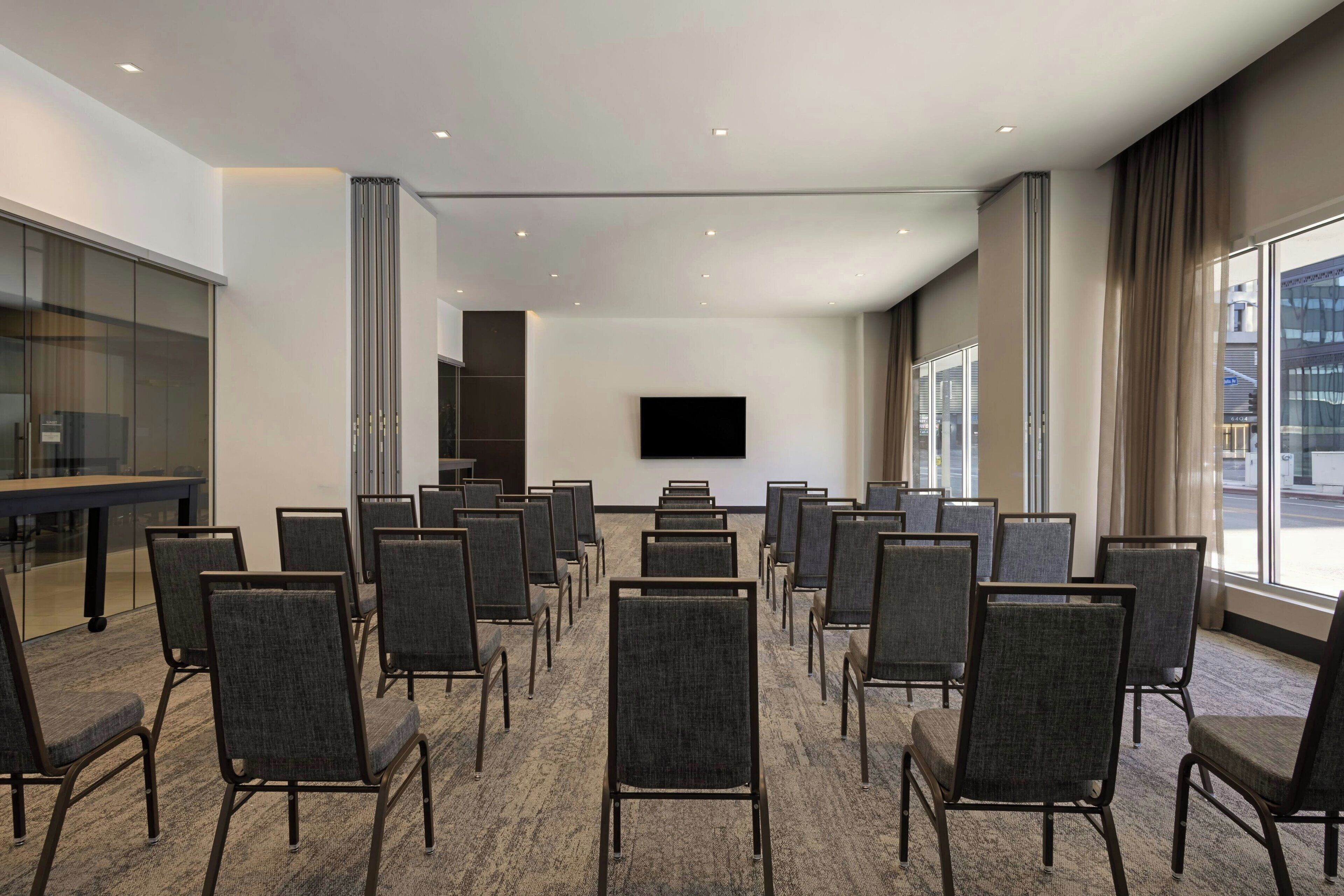 A conference room with rows of chairs, a flat-screen TV, and large windows offering a view of the outside.