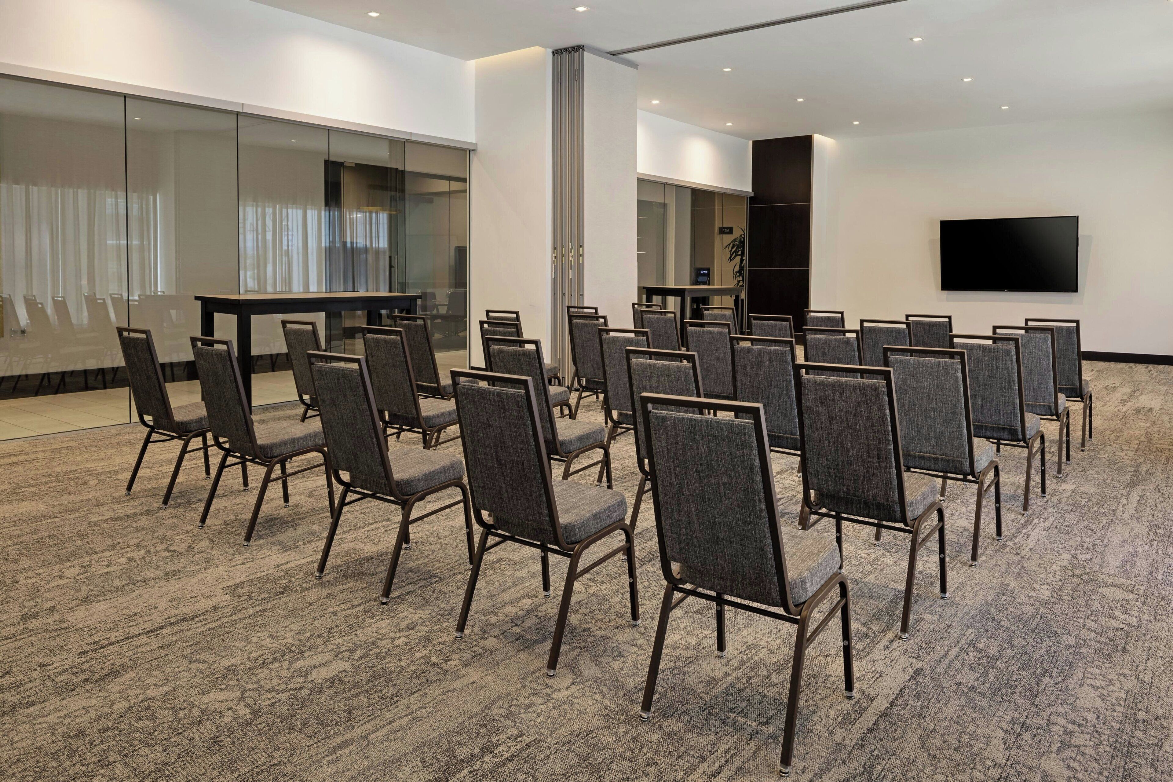Een vergaderzaal met rijen stoelen, een grote tafel, een flatscreen-tv en glazen wanden.
