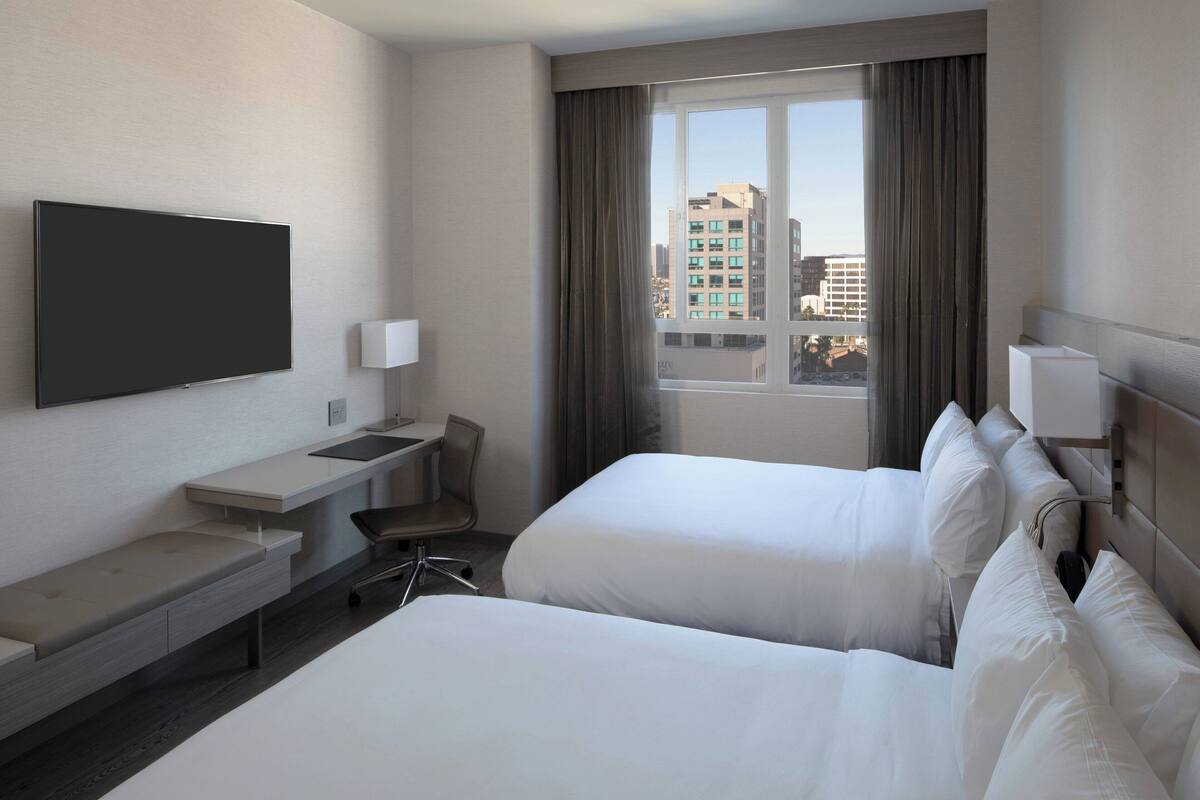 Une chambre d’hôtel avec deux lits, un bureau, une chaise et un téléviseur.