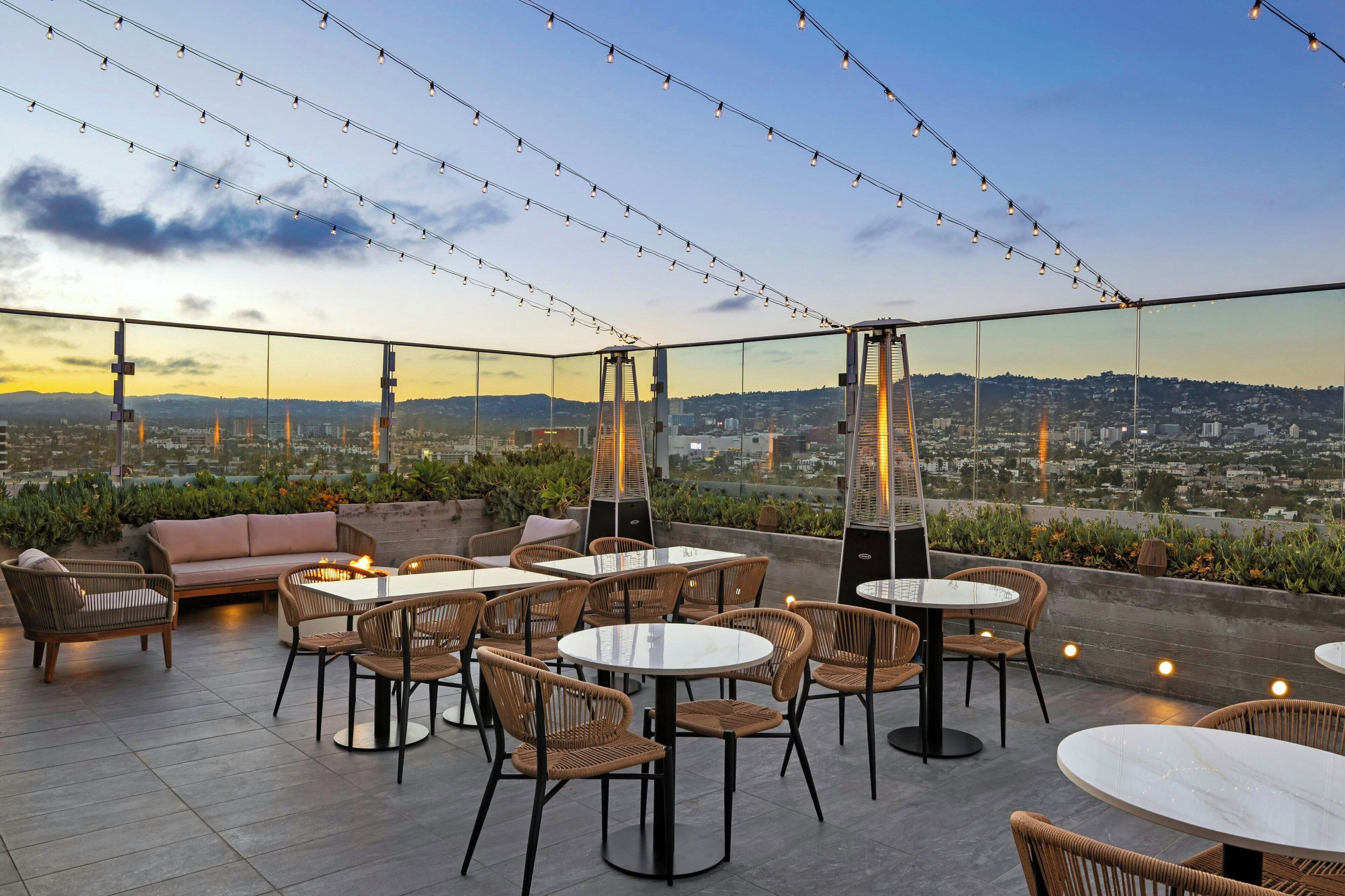 An outdoor seating area with wicker chairs and tables, string lights, and a city view.