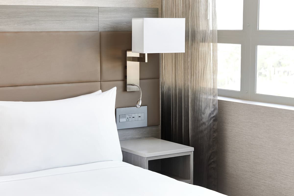Une chambre d’hôtel moderne équipée d’un lit, d’une table de chevet, d’une lampe et d’une prise de courant.