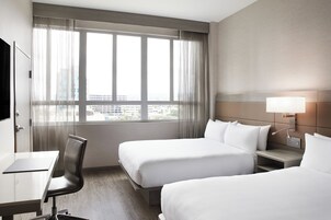 Quarto de hotel com duas camas, uma escrivaninha e uma cadeira.