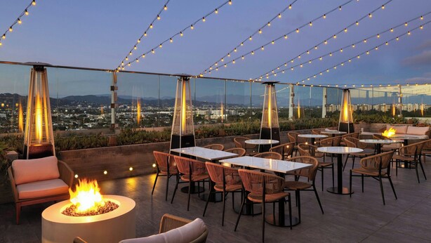Een terras met tafels, stoelen, een vuurplaats en sfeerverlichting.