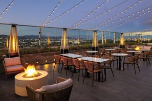 Un espace extérieur aménagé avec des tables et des chaises, un foyer et des guirlandes lumineuses.