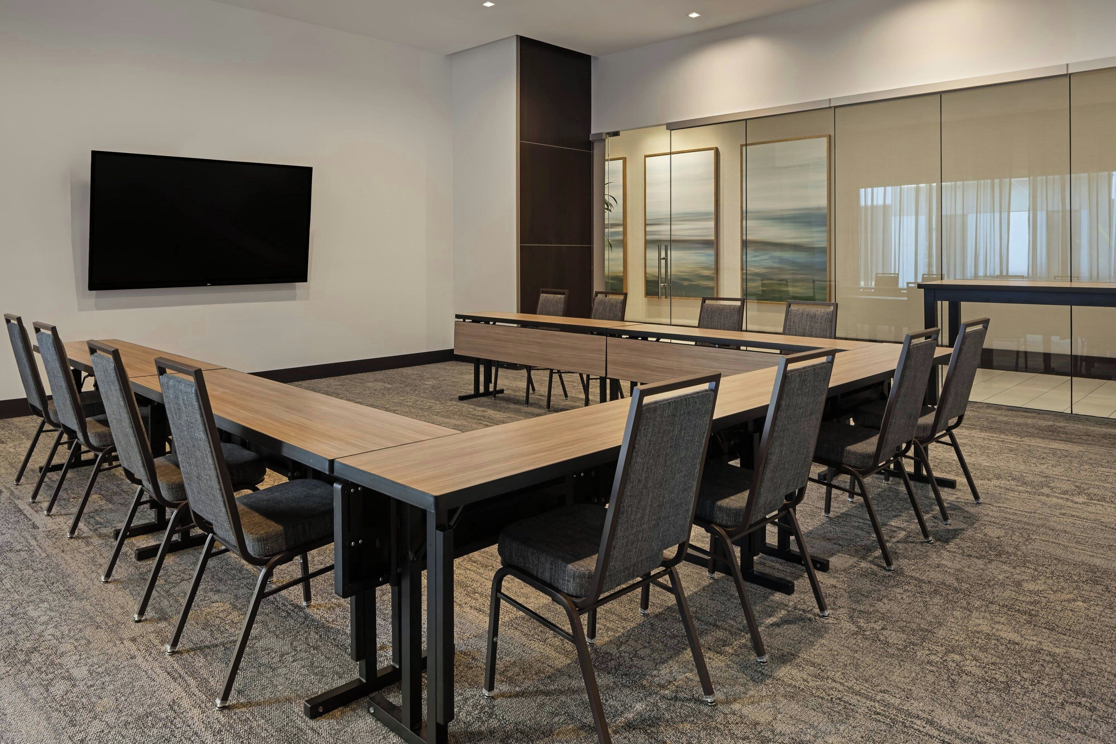 A conference room with a long table, chairs, a flat-screen TV, and a glass partition with a view.