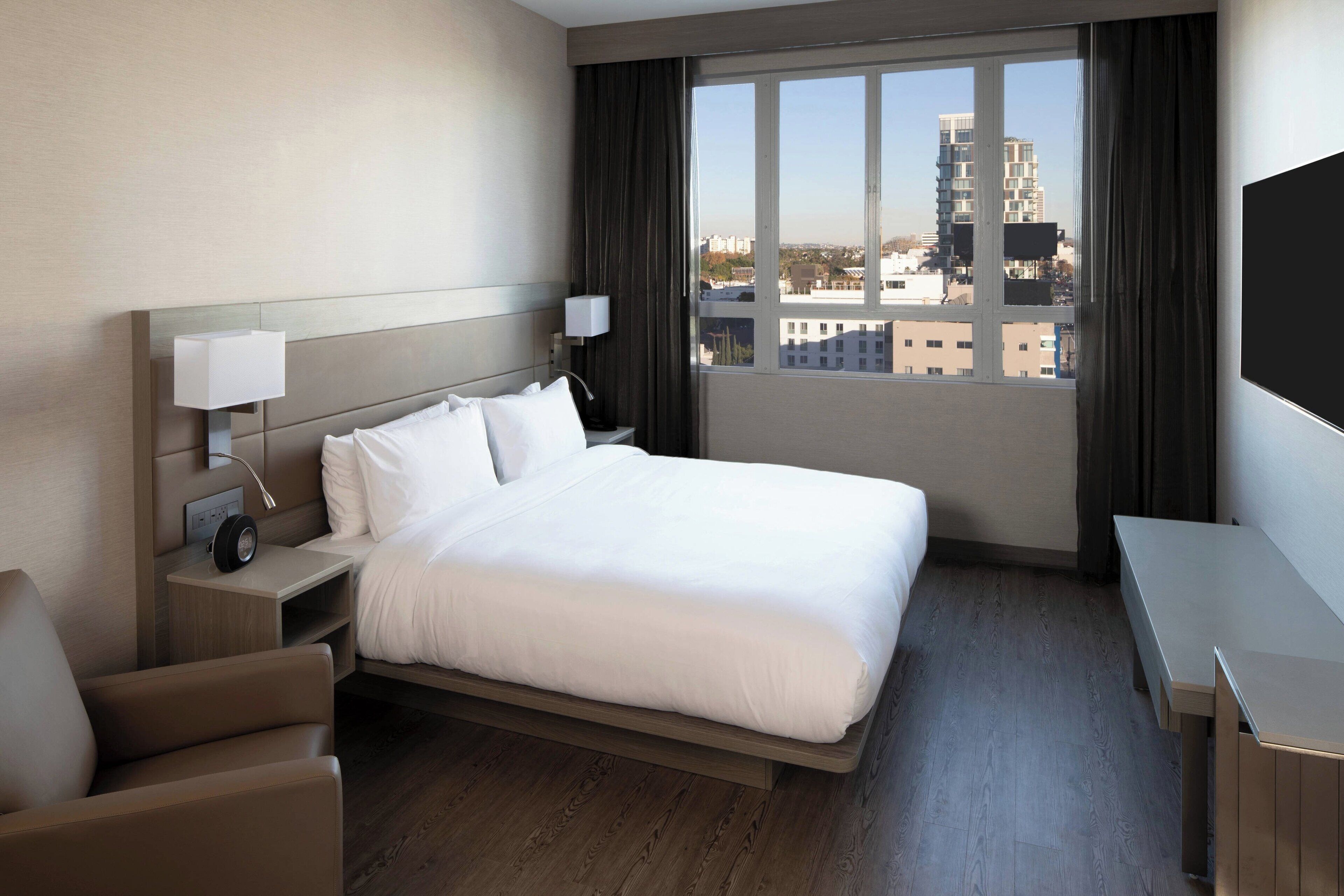 A hotel room with a large bed, bedside tables, a desk, and a view of the city.
