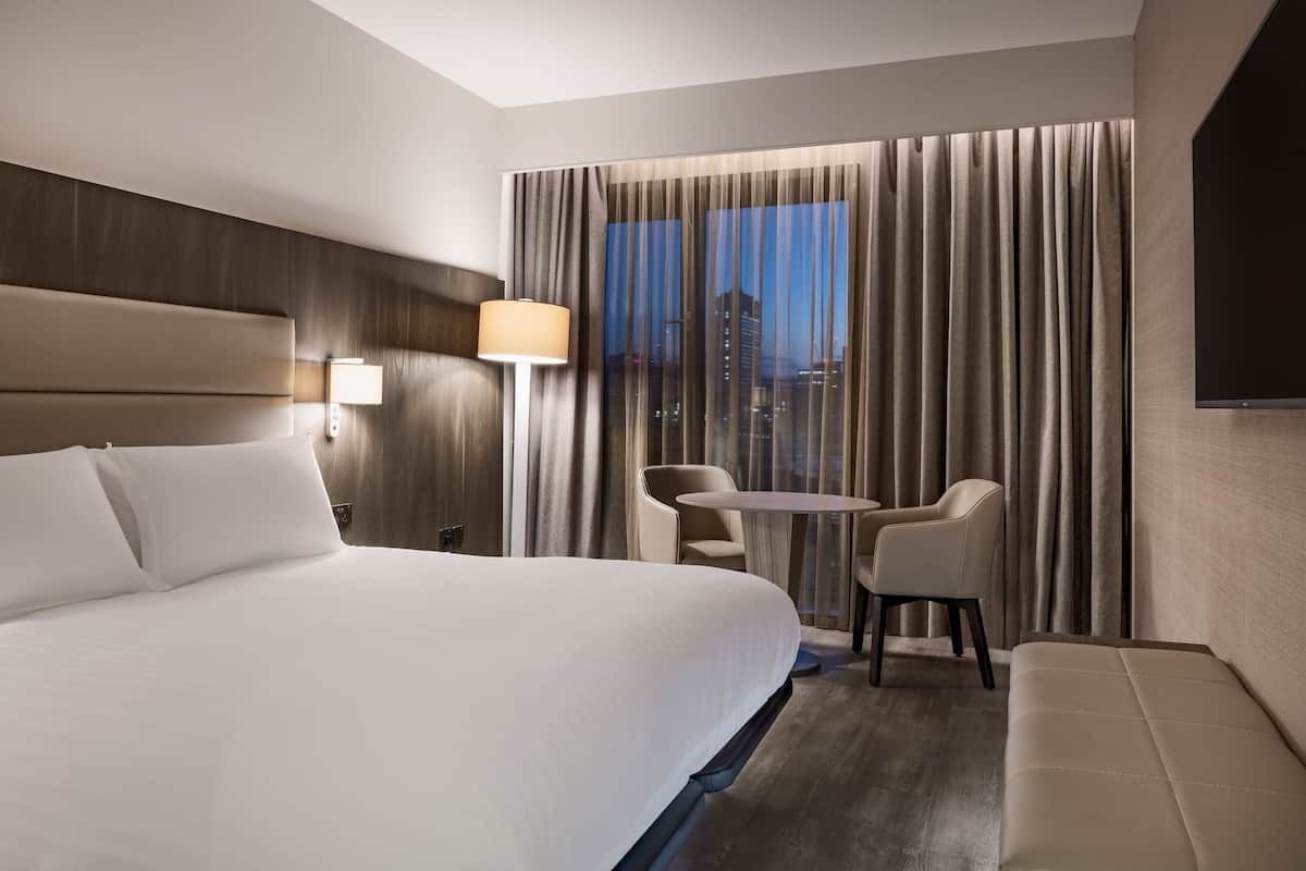 Ein Hotelzimmer mit einem großen Bett, einem Schreibtisch, einem Sessel und einem Fernseher.
