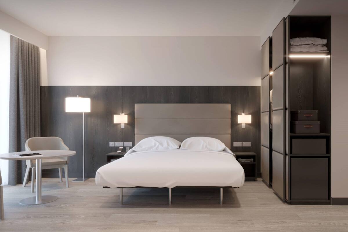 Ein modernes Hotelzimmer mit einem großen Bett, Nachttischen, einem Schreibtisch und einem Kleiderschrank.