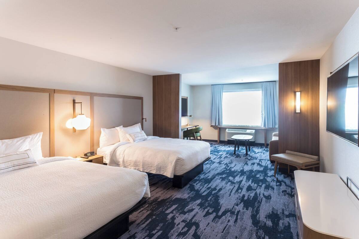 A hotel room with two beds, a desk, a chair, and a TV.